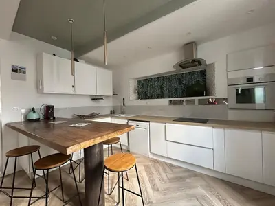 a kitchen with white cabinets and a wooden table with stools at Maison chaleureuse atypique in Saint-Chinian