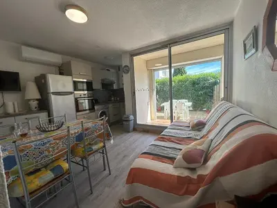 a bedroom with a bed and a kitchen with a window at Le Ponant - Appartement proche du port et de la mer in Gruissan