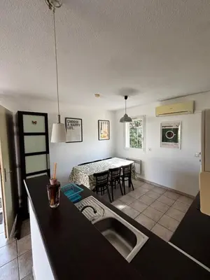 a kitchen and living room with a sink and a table at Résidence Les jardins du Phoebus Géolia Piscine Climatisation Parking By LCG in Gruissan