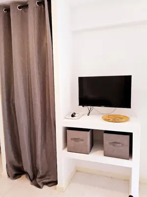 a tv on a white stand with a curtain at L'anguille du port clim jardin mer in Port-la-Nouvelle