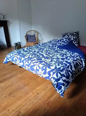 a bed with a blue and white blanket on a wooden floor at Chambre b&b in Miraval-Cabardès