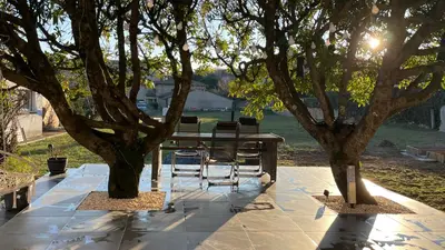 a table and chairs sitting under two trees at LE HAVRE D'ATHENA - Grand appart, jardin privé, abri vélos & accès rapide A61 in Castelnaudary
