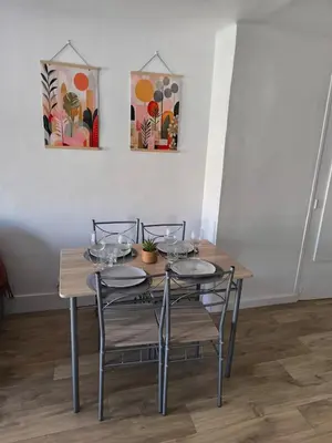 a wooden table with four chairs and paintings on the wall at Bel Appartement Terracotta au cœur de Narbonne in Narbonne
