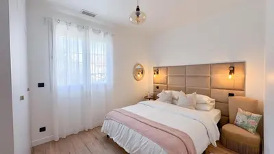 a white bedroom with a large bed and a chair at Maison Climatisée 5min Cité Terrasse et Parking AK in Carcassonne