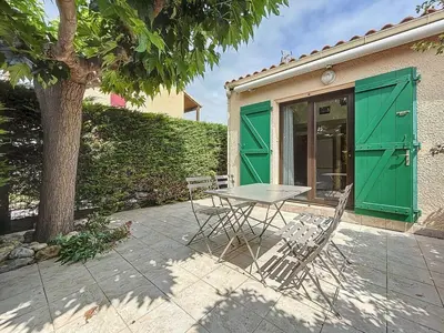 a table and chairs in front of a building with green doors at La Feuilleraie - Maison de vacance à Leucate in Leucate
