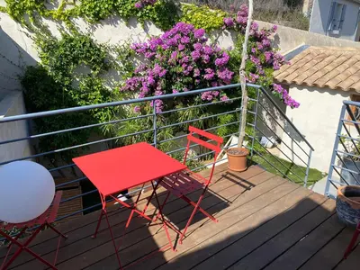 two chairs and a red table on a deck with flowers at Maison bougainvillier Gruissan Village in Gruissan