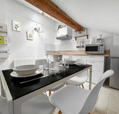a kitchen with a black counter and white chairs at Appartement Lumineux Carcassonne Centre in Carcassonne