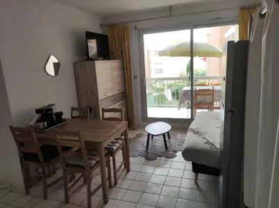 a living room with a table and chairs and a window at 2 appartements mitoyens avec climatisation, piscine et parking - Plages et Port à 100m in Gruissan