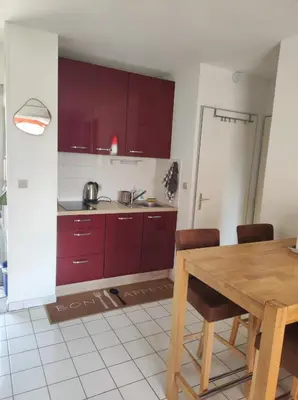 a kitchen with red cabinets and a wooden table at 2 appartements mitoyens avec climatisation, piscine et parking - Plages et Port à 100m in Gruissan