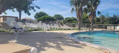 a group of chairs and a swimming pool with palm trees at Mobile Home climatisé 2 chambres Port La Nouvelle in Port-la-Nouvelle