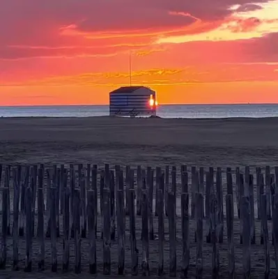 a sunset on the beach with a building on the beach at Ondine in Gruissan