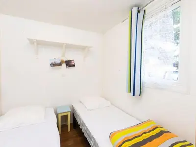 two beds in a small room with a window at Mobil-home avec Terrasse à Lézignan-Corbières, 6 personnes - API-1-52-736 in Lézignan-Corbières