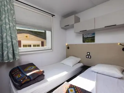 two beds in a small room with a window at Mobil home spacieux avec terrasse pour 8 personnes - API-1-52-793 in Lézignan-Corbières