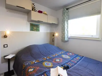 a bedroom with a bed with a blue comforter and a window at Mobil home spacieux avec terrasse pour 8 personnes - API-1-52-793 in Lézignan-Corbières