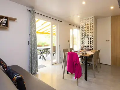 a dining room and living room with a table and chairs at Mobil home spacieux avec terrasse pour 8 personnes - API-1-52-793 in Lézignan-Corbières
