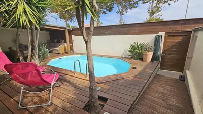 a swimming pool on a wooden deck with a red chair at Villa Standing Piscine Chauffée in Gruissan