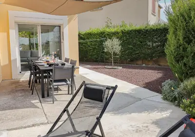 a dining table and chairs in a backyard with an umbrella at L'Escapade Jaune - Jacuzzi, Wi-Fi, tout équipée in Carcassonne