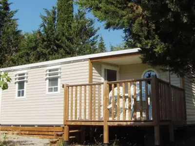 a small white house with a large wooden deck at Mobil-home confortable avec terrasse - API-1-52-652 in Lézignan-Corbières