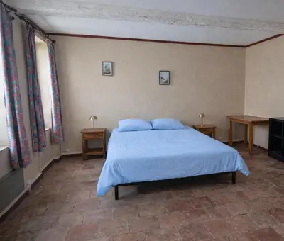 a bedroom with a bed with blue sheets and two tables at Charmante maison de village à Tourouzelle in Tourouzelle