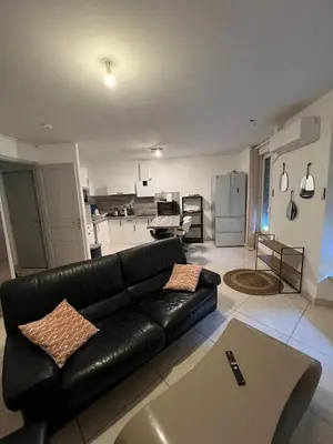 a living room with a black leather couch and a kitchen at T2 apartment, terrasse cours intérieur in Narbonne