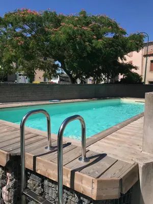 a pool with a wooden boardwalk next to a swimming pool at l'Ecrit Vin in Rustiques