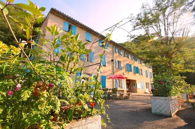 a building with blue shutters and flowers in front of it at Auberge de jeunesse La Forge in Quillan