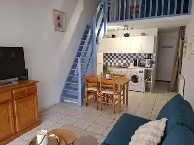 a living room with a table and a blue staircase at Appartement T2 entre mer et lac in Port-la-Nouvelle