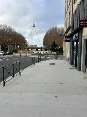a sidewalk with a street with a windmill in the background at Les berges de la cité in Carcassonne