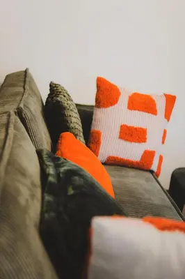 a person sitting on a couch with orange and white pillows at T2 cosy tout équipé, parking et wifi gratuit, Castres in Castres