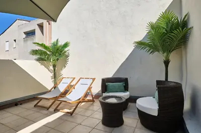 a balcony with chairs and palm trees on a building at Bel Appartement Climatisé avec Terrasse au centre-ville de Narbonne in Narbonne