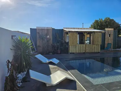 a swimming pool with two white chairs next to a house at Studio Conteneur in Cruscades