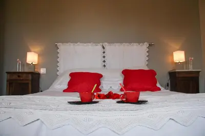 a white bed with two red pillows and red glasses on it at L'Oustal d'en Paris in Nogaret