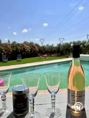 a bottle of wine and glasses on a table with a pool at Le gite aux oliviers in La Redorte