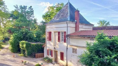 an old white house with a tower and red windows at Gite Charles de Castres in Saint-Affrique-les-Montagnes