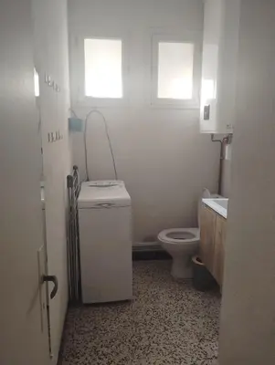 a bathroom with a toilet and a sink and two windows at Appartement bord de mer in Port-la-Nouvelle