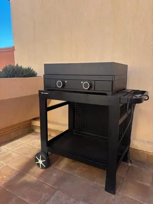 a black grill sitting on a cart next to a wall at Elégant T3, vue sur le port - Grande terrasse in Gruissan
