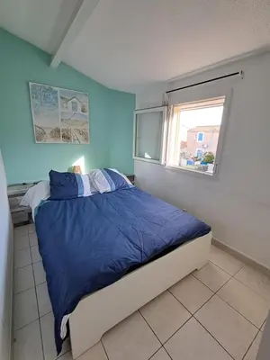 a bedroom with a bed with blue sheets and a window at location maison gruissan in Gruissan