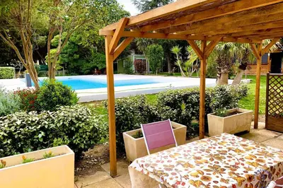 a wooden pergola with a table and chairs next to a pool at Gîte Piscine in Narbonne