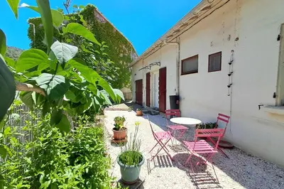 a patio with red chairs and a table and a building at L'évasion des Corbières in Portel-des-Corbières