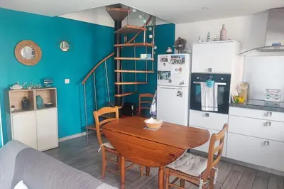 a kitchen with a table and a refrigerator and a staircase at Lo Cabanot maison de pêcheur pour 4 in Port-la-Nouvelle