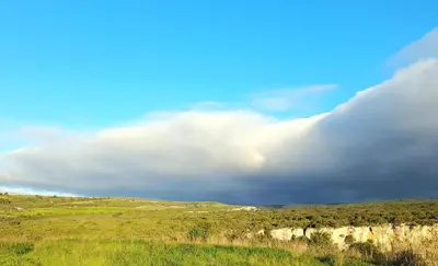 a cloudy sky over a grassy field with trees and a hill at Maison entre mer et montagne in Cassagnolles