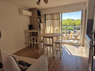 a living room with a table and chairs and a window at Les pieds dans l'eau Studio Cabine terrasse, refait à neuf 5 minutes plage à pied climatisé in Gruissan
