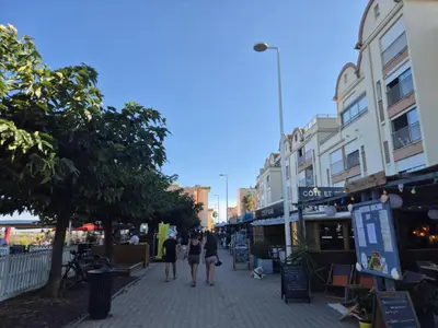 a group of people walking down a street with buildings at Les pieds dans l'eau Studio Cabine terrasse, refait à neuf 5 minutes plage à pied climatisé in Gruissan