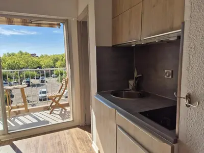 a kitchen with a sink and a balcony with a view at Les pieds dans l'eau Studio Cabine terrasse, refait à neuf 5 minutes plage à pied climatisé in Gruissan