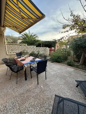 a patio with a table and chairs under a umbrella at Pavillon moderne & spacieux - accès direct plage in Gruissan