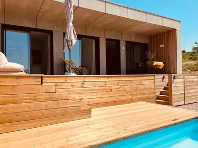 a house with a wooden deck next to a swimming pool at Plein Soleil in Félines-Minervois