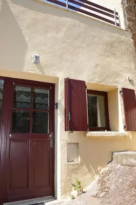 a house with a red door and two windows at Gite La Grange, climatisée, vue sur le château de Peyrepertuse in Rouffiac-des-Corbières