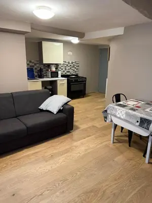 a living room with a black couch and a kitchen at Appartement détente dans les corbières in Conilhac-Corbières