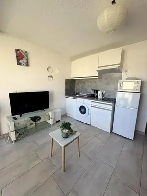 a kitchen with white appliances and a table in a room at Studio à deux pas du port avec piscine in Gruissan