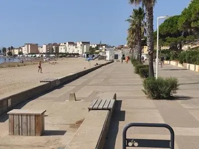 a beach with benches and people walking on the beach at Studio à 50m de la Plage du Grazel avec Parking - FR-1-796-104 in Gruissan